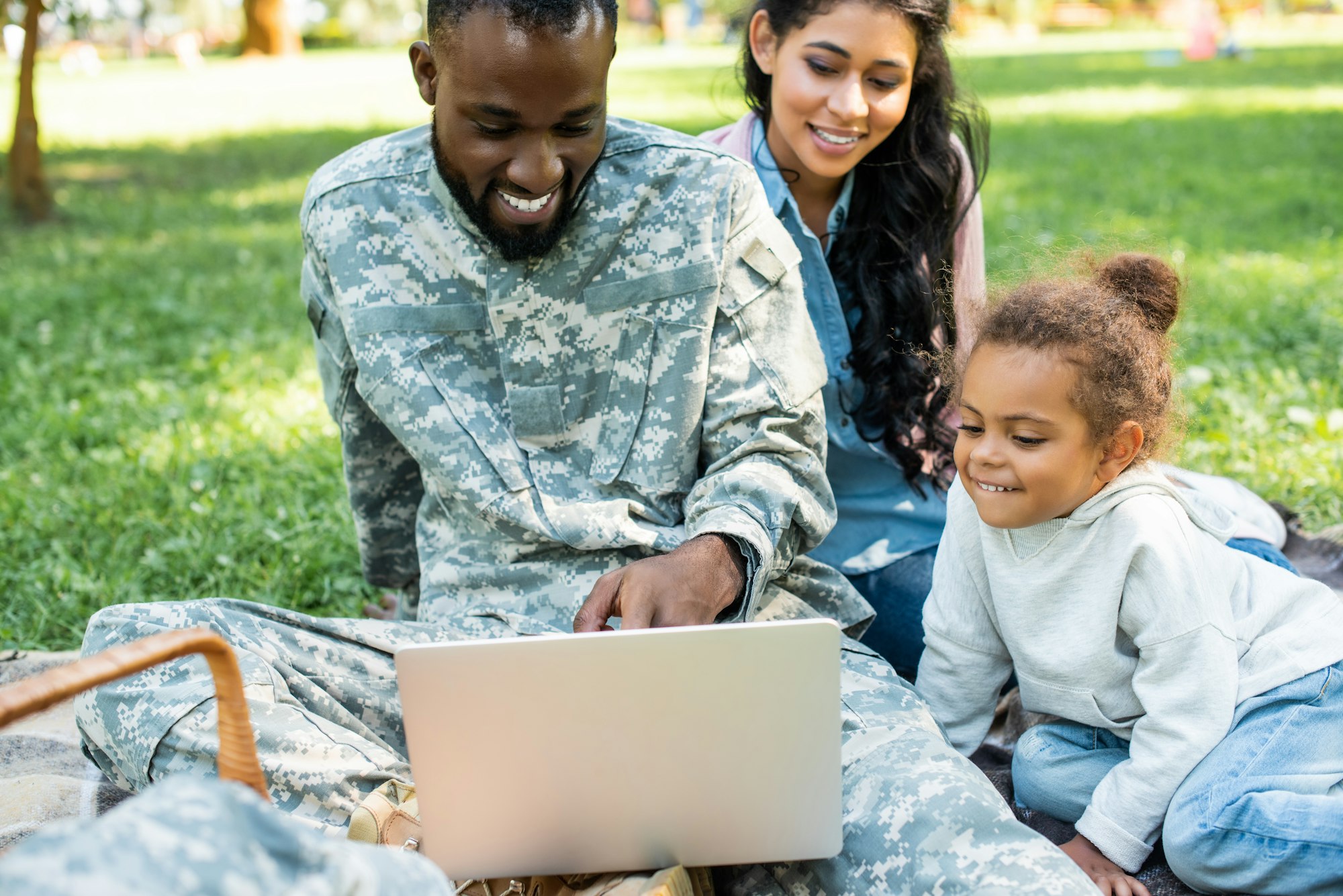 smiling african american soldier in military uniform using laptop with family in park